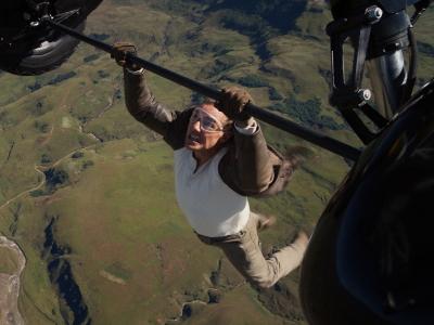 Tom Cruise hænger fra en flyvemaskine højt over jorden.